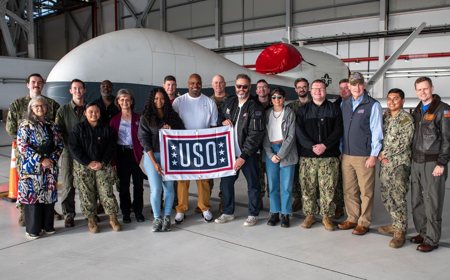 U.S. Navy Adm. Christopher Grady and an ensemble of celebrities pose for a photo with service members