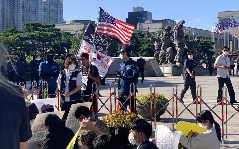 A group of anti-war protesters sit in front of the War Memorial Hall of Korea as a counter-demonstrator and police survey the scene in Seoul, South Korea, Aug. 27, 2022.