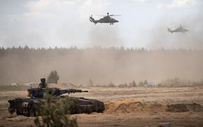 A tank and two helicopters move through a dusty field with a forest in the background.