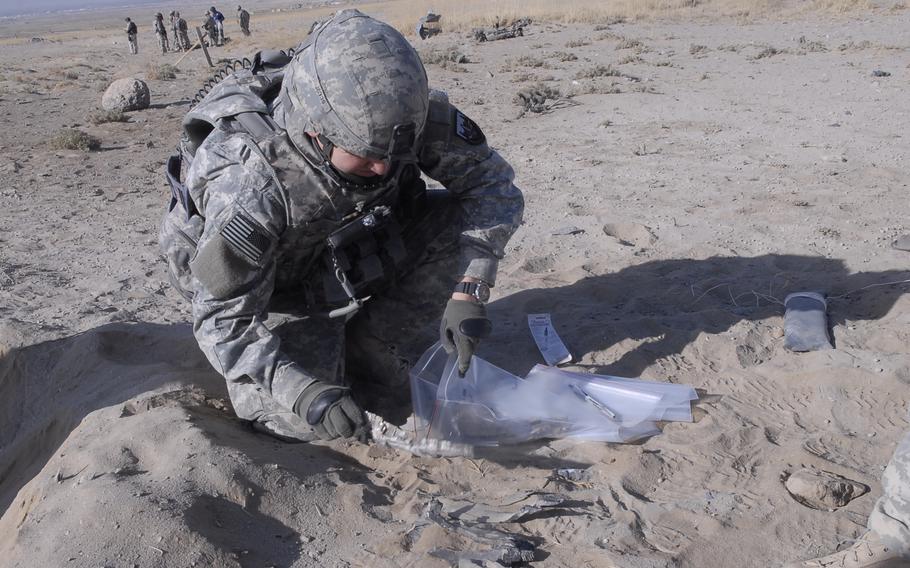 A soldier crouches to handle debris and place it into a bag.