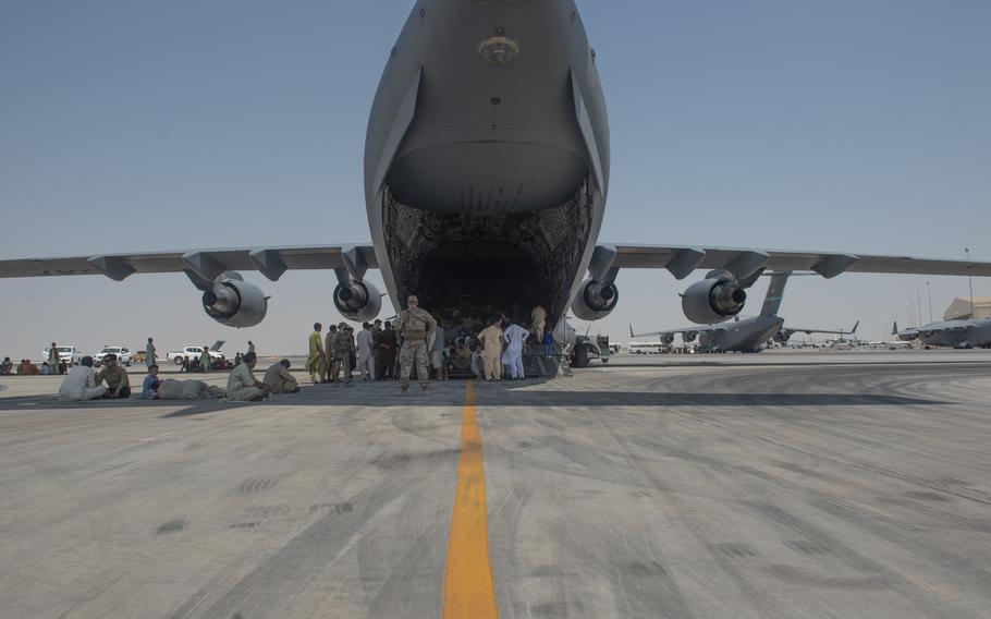 Evacuees wait under the wing of C-17 Globemaster lll after arriving in an undisclosed location in the Middle East region on Friday, Aug. 20, 2021, after being evacuated onboard a military aircraft from Hamid Karzai International Airport in Kabul, Afghanistan, as part of Operation Allies Refuge. 