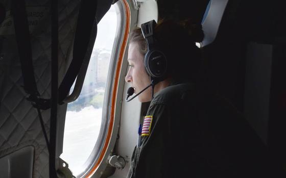 A Coast Guard flight crew member looks out the window as she's positioned to watch for any danger on a flight to Southwest Florida on Sunday, Oct. 2, 2022. 