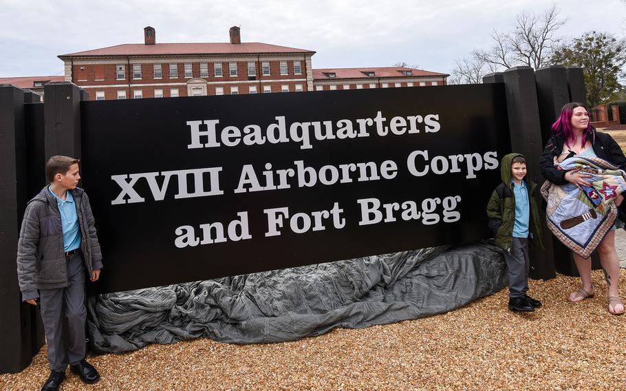 A woman and two boys stand on either side of a brown welcome sign reading “Headquarters XVIII Airborne Corps and Fort Bragg.”