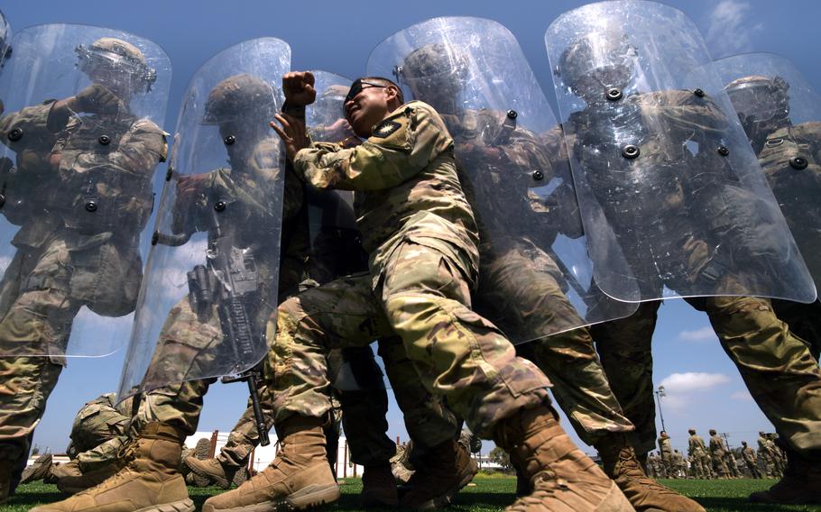 Soldier pushes against shields being held by other soldiers.