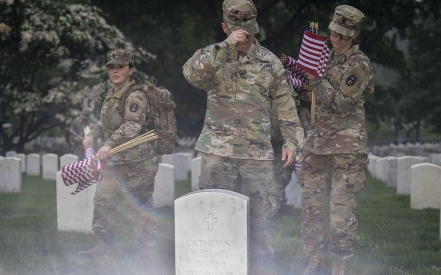Soldiers prepare to place flags at headstones.