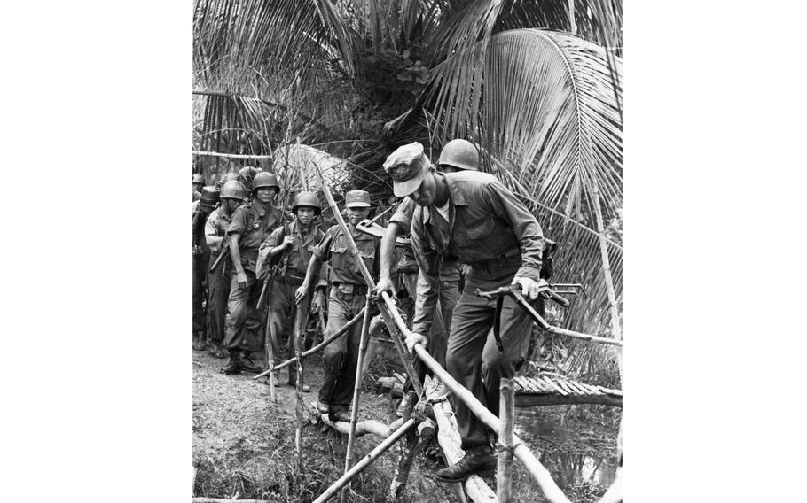 Soldiers walk across a bamboo footbridge