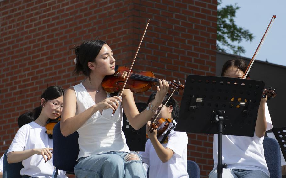 Teenagers in a youth orchestra play violin outside.