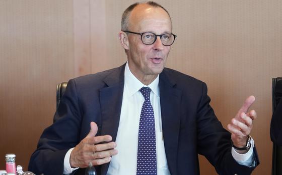 Friedrich Merz in a suit, gesturing with both hands and speaking.