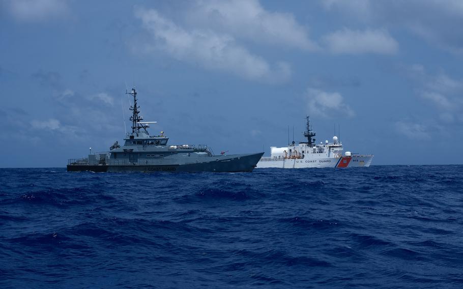 A Coast Guard vessel and a Coast Guard cutter sail next to each other on the water.