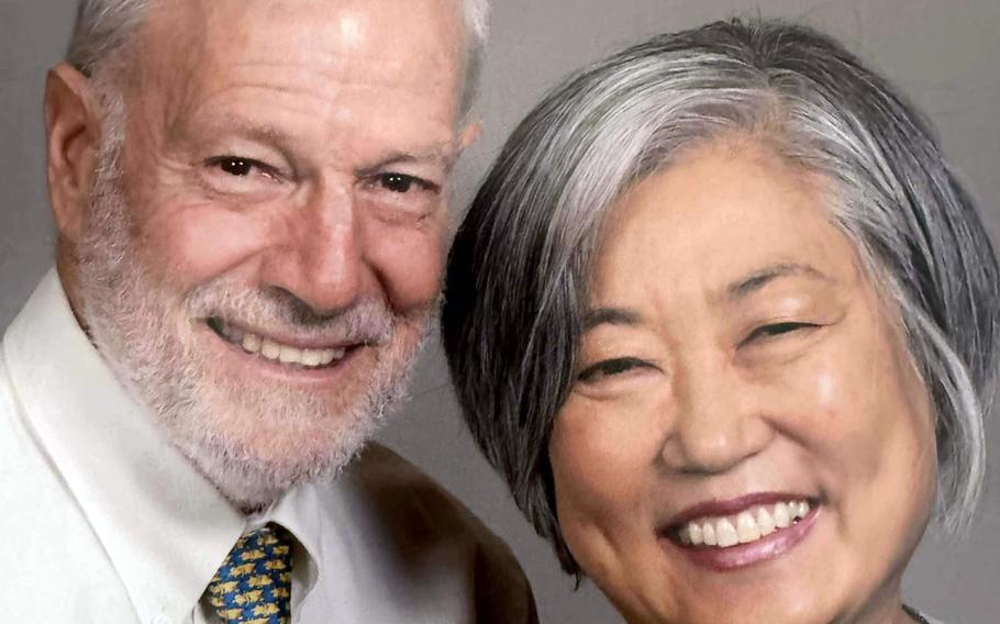 An elderly couple, seen from the neck up, smile while looking forward and posing.