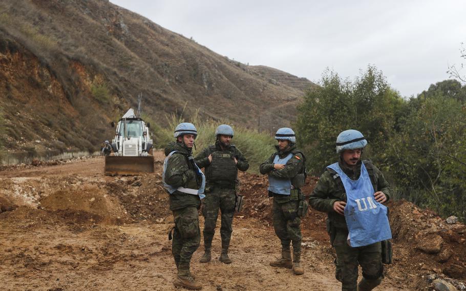 U.N. peacekeepers stand outside wearing blue vests and helmets.