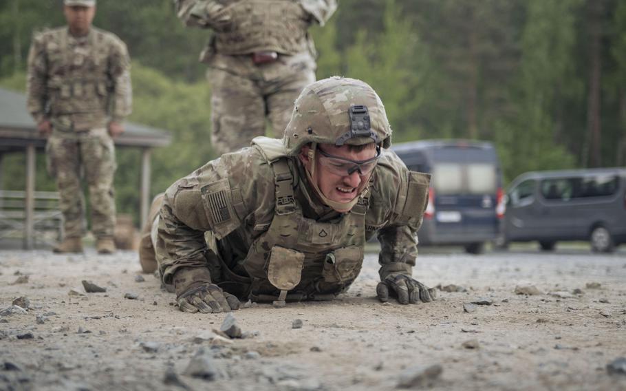 A soldier doing pushups, as seen from his front, with two other standing behind him.