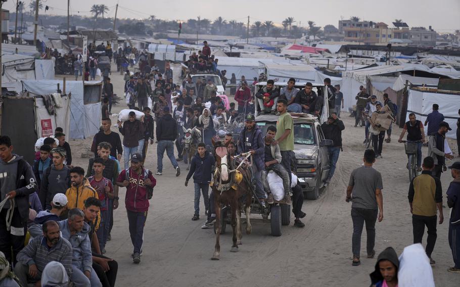 Palestinians walk past tents, with some carrying bags of aid.