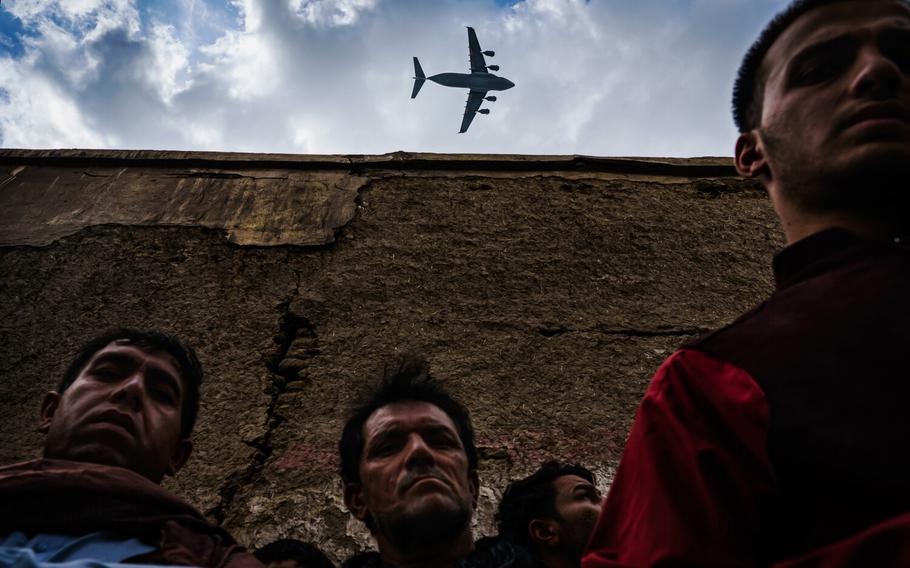 A military transport plane flies over relatives and neighbors of the Ahmadi family as they gather around an incinerated husk of a vehicle destroyed by a U.S. drone strike in Kabul, Afghanistan. In August 2021, life came to a standstill as the Taliban offensive reached the gates of the Afghan capital, sending it into a panic. President Ashraf Ghani escaped; American-backed Afghan forces pulled back. The Taliban swiftly took over a nation that had changed much since it first ruled two decades ago. Jarring, violent scenes followed, marking a tragic coda to a messy and controversial 20-year occupation. The U.S. was ending its longest war.