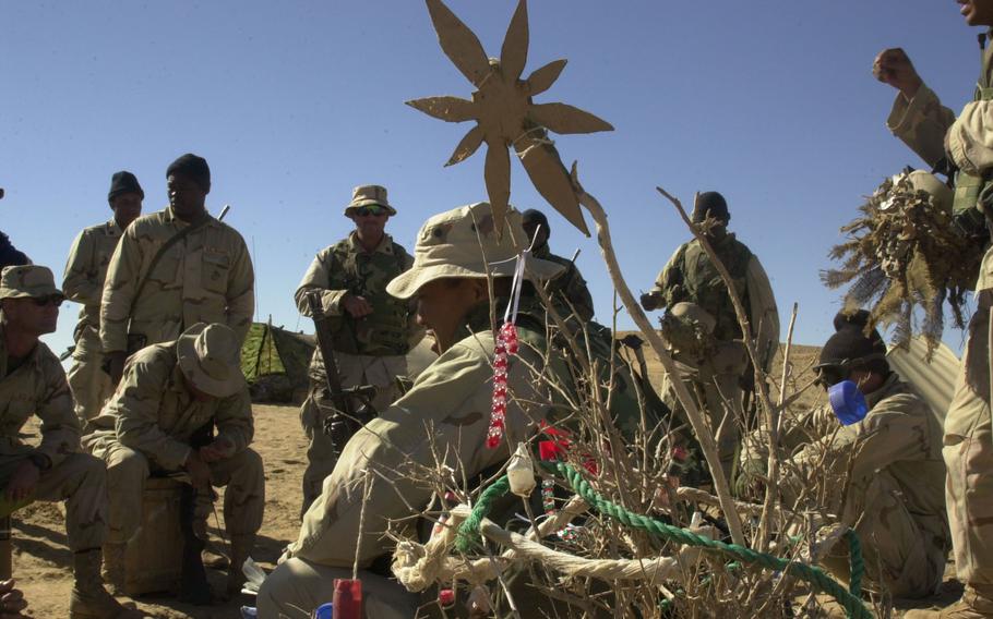 Despite living in a war zone, Marines at Camp Rhino, Afghanistan, display their holiday spirit, Dec. 12, 2001. The desert version of a Christmas tree — dried brush decorated with bits of rope and red-and-white beaded candy cane, complete with a star on top — provided a quirky backdrop for the troops’ morning briefings. The Marines at Camp Rhino were the first major U.S. ground component in the war in Afghanistan.