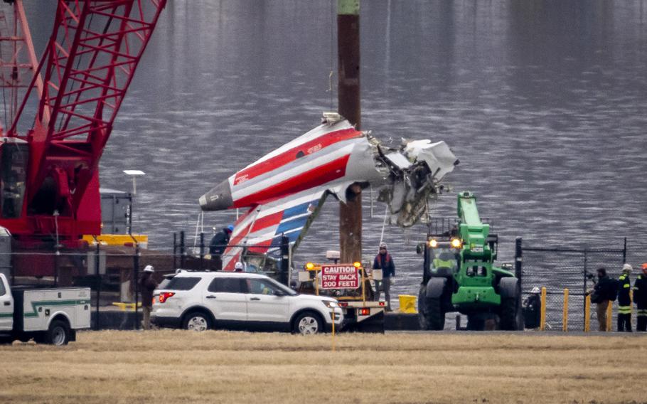 A red crane on the shore of a river lifts a piece of a jetliner with a red, white and blue U.S. flag paint scheme from the water during a salvage operation.