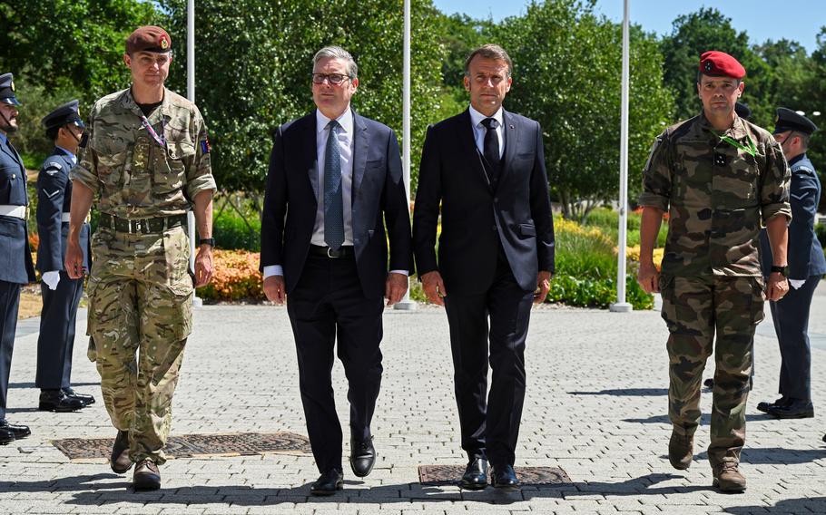 The leaders of the U.K. and France walking side by side in suits as service members walk on either side of them.