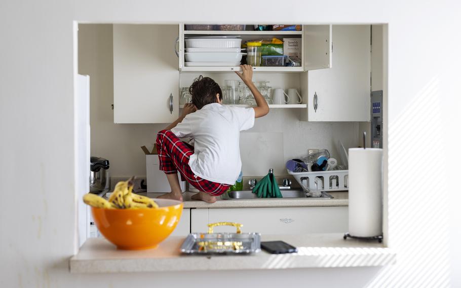 A young Afghan refugee climbs onto the counter of his family's new apartment in Rochester, N.Y., to get a snack on June 13, 2022. The child's father was an interpreter for U.S. troops in Afghanistan who was able to relocate to the United States with his wife and two children. 