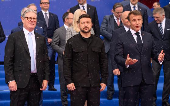 Keir Starmer, Volodymyr Zelenskyy and Emmanuel Macron stand next to each other in a row in front of other government officials on blue-carpeted steps during a photo op.
