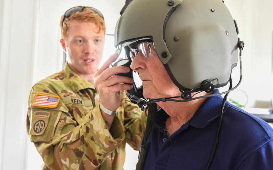 A man tries on a pilot’s helmet as a soldier helps him.