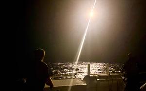 Coast Guard crew members send up a bright flare into a dark sky. 