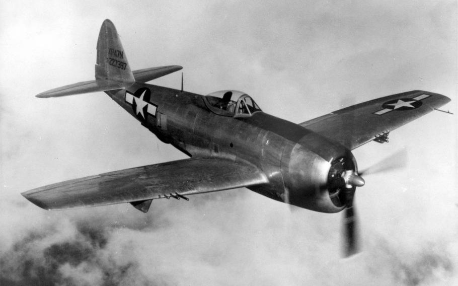 A black-and-white, 1940s-era image of a World War II airplane flying in the air with clouds behind it.
