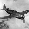 A black-and-white, 1940s-era image of a World War II airplane flying in the air with clouds behind it.