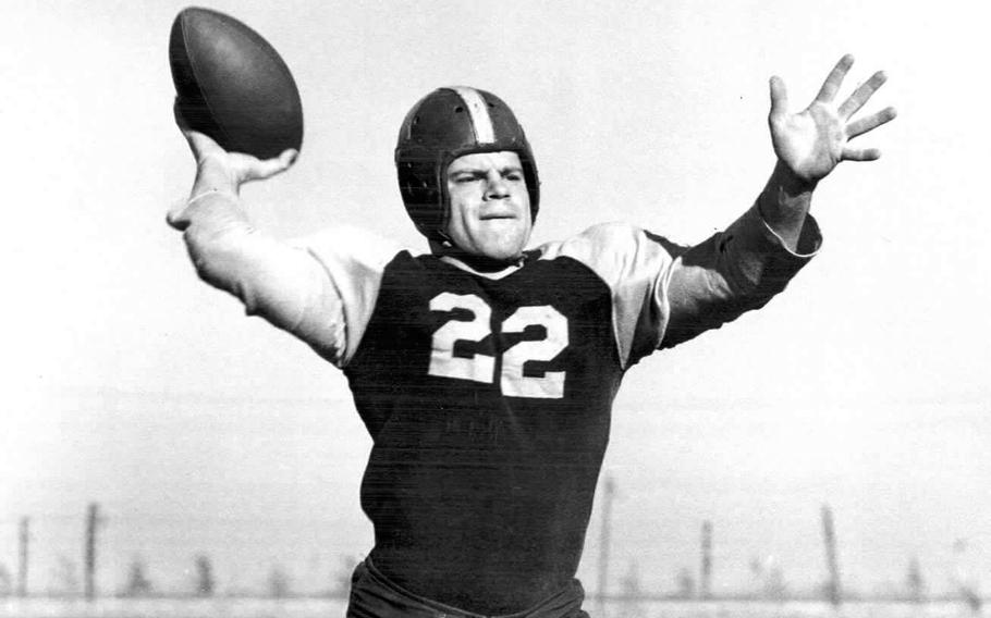 A black and white photo of a football player with both hands raised, one gripping a football.