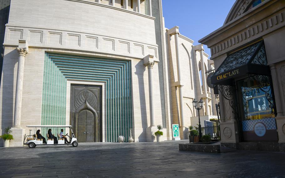 A golf cart shuttles tourists around Katara Cultural Village in Doha, Qatar, and passes the entrance to the district amphitheater as well as a luxury chocolate shop on Oct. 1, 2022.