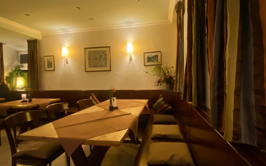 The Oelmuehle restaurant’s dining room is well-apportioned with wood. The chocolate brown table settings are combined with drapes of assorted hues and brightly colored pillows and cushions on the dining room bench. 