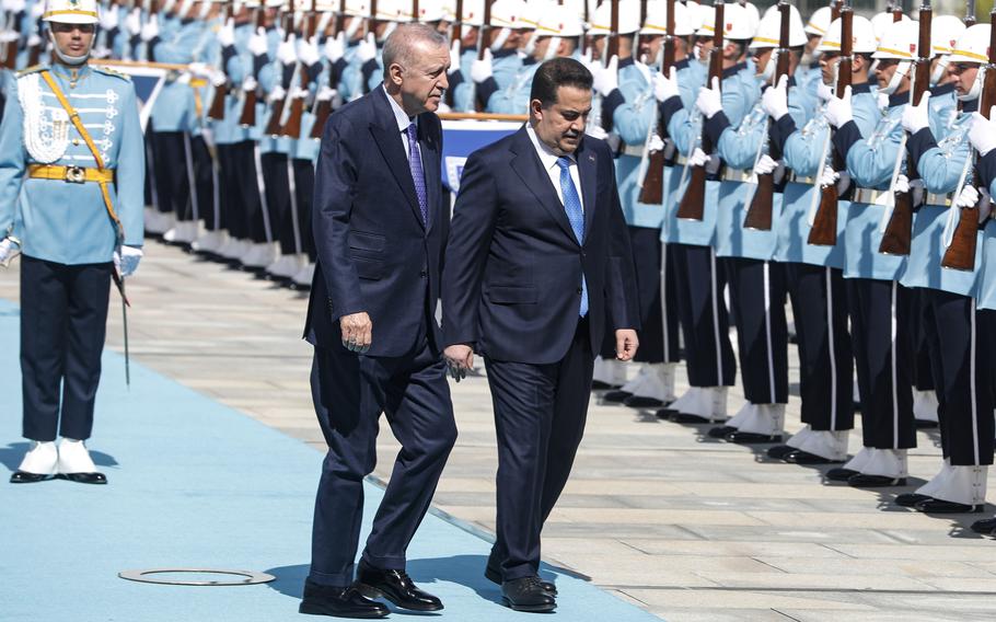 Two men in suits walk down a blue carpet, in front of an honor guard.