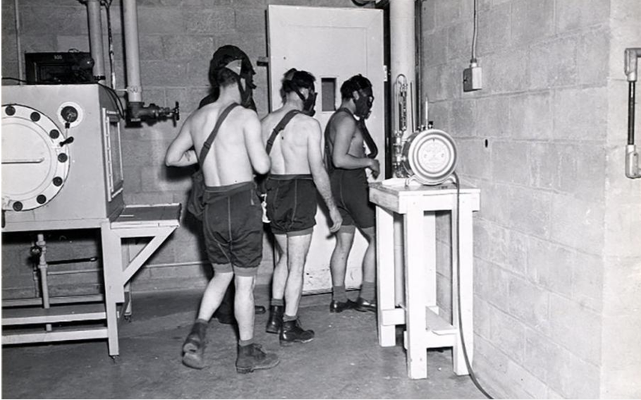 Three shirtless men wearing shorts and face masks are walking through a doorway.