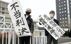 Plaintiff Katsuhiro Hirano, right, and unidentified lawyer for the plaintiffs display signs after a judgement at Hiroshima District Court in Hiroshima, western Japan Tuesday, Feb. 7, 2023. The banners read " Pave the way to backup Second-Generation Atomic Bomb Survivors," right, and " Unfair judgement." (Kyodo News via AP)