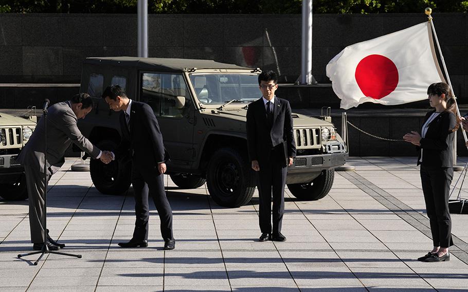 Sergiy Korsunsky, center, Ambassador of Ukraine to Japan, left, and Toshiro Ino, second left, state minister of Defense of Japan, shake hands during the handover ceremony of defense equipment for Ukraine at the Ministry of Defense Wednesday, May 24, 2023, in Tokyo. Japan Ground Self-Defense Force’s the 1/2-ton trucks, seen in background, are part of handover defense equipment. 