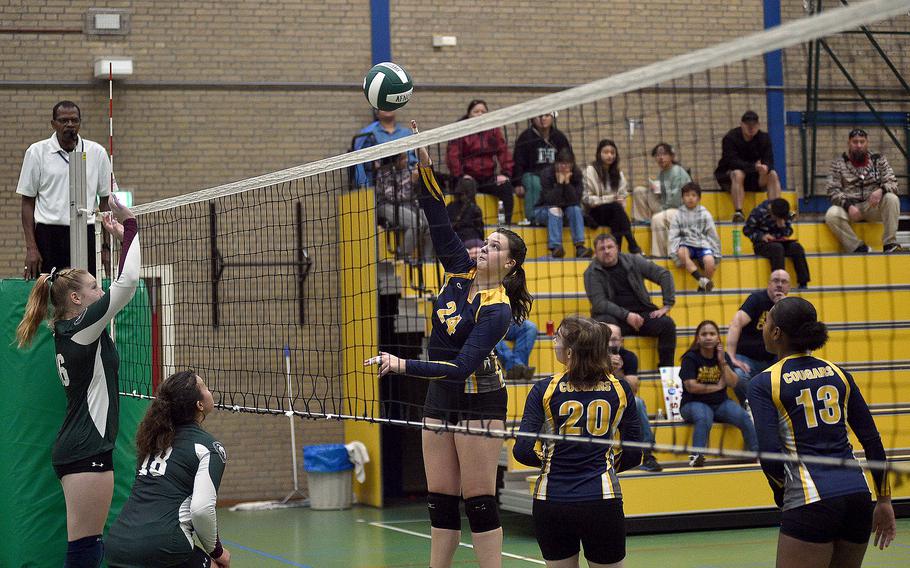 Ansbach sophomore Kennedy Lange goes to spike the ball in a match against the Lions on Oct. 7, 2023, at AFNORTH in Brunssum, Netherlands. going up for the block are, from left, the Lions' Adelle Bown and Bella Benedetto.