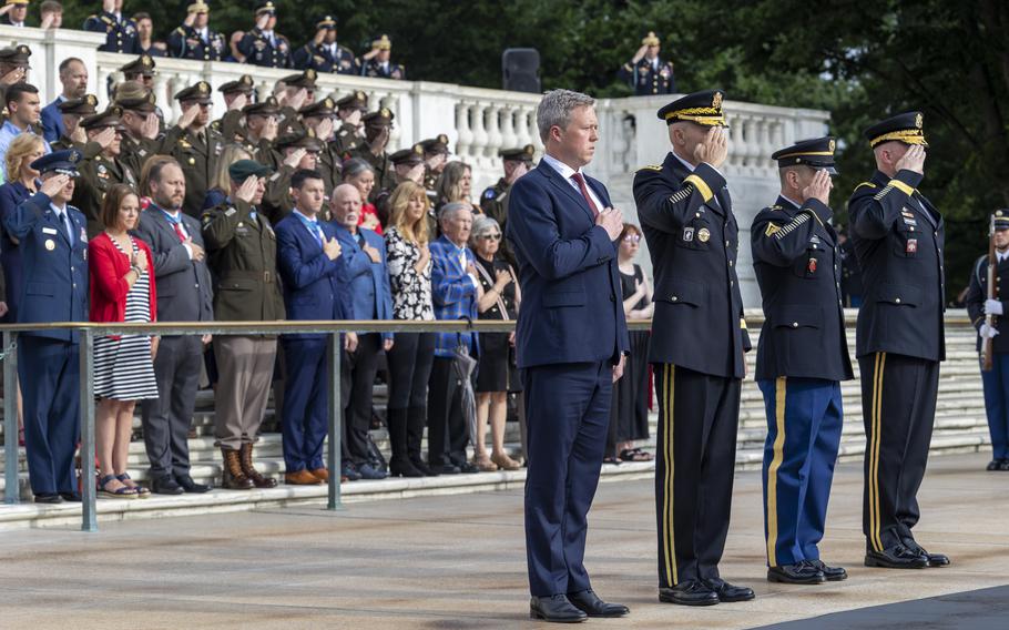 Army leaders and others stand at attention, some saluting, others with their  right hand over their heart during a ceremony.