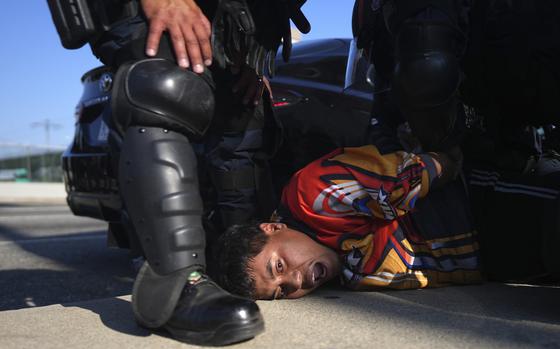 A protester seen exclaiming as he is confined by a kneeling law enforcement officer.