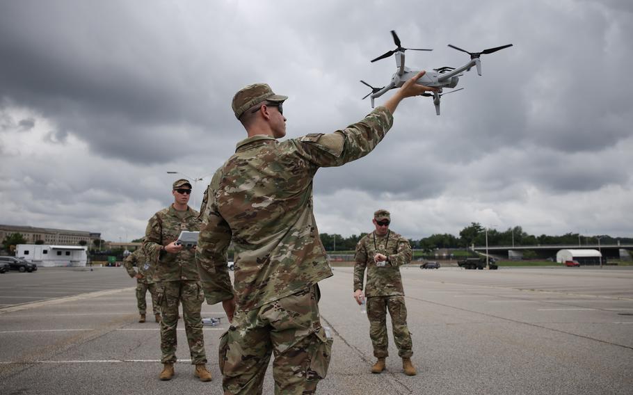 Several soldiers in a parking lot on a cloudy day, one of whom is holding a drone above his head.