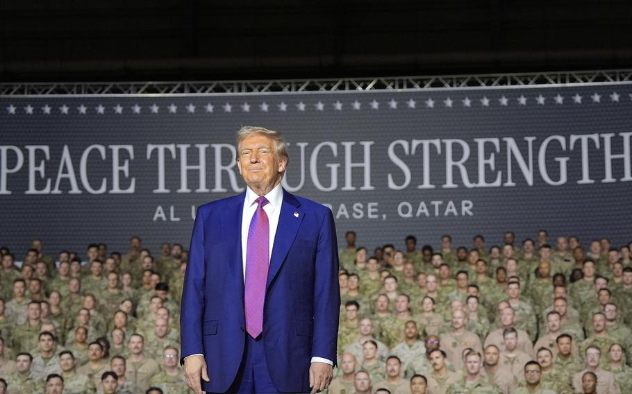 President Trump stands and smiles slightly in a blue suit, with rows of military personnel behind him in the background.