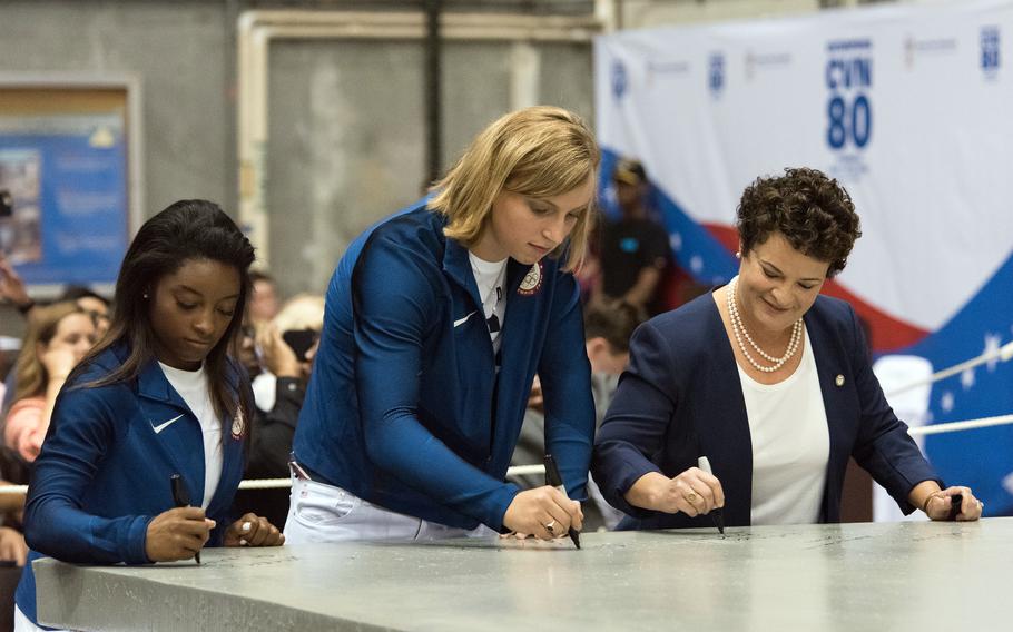 Olympic gold medalists Simone Biles, left, and Katie Ledecky, ship’s sponsors of the future aircraft carrier USS Enterprise, and Jennifer Boykin, president of Newport News Shipbuilding, sign a 35-ton steel plate to start advance construction of Enterprise in Newport News, Va., Aug. 24, 2017.