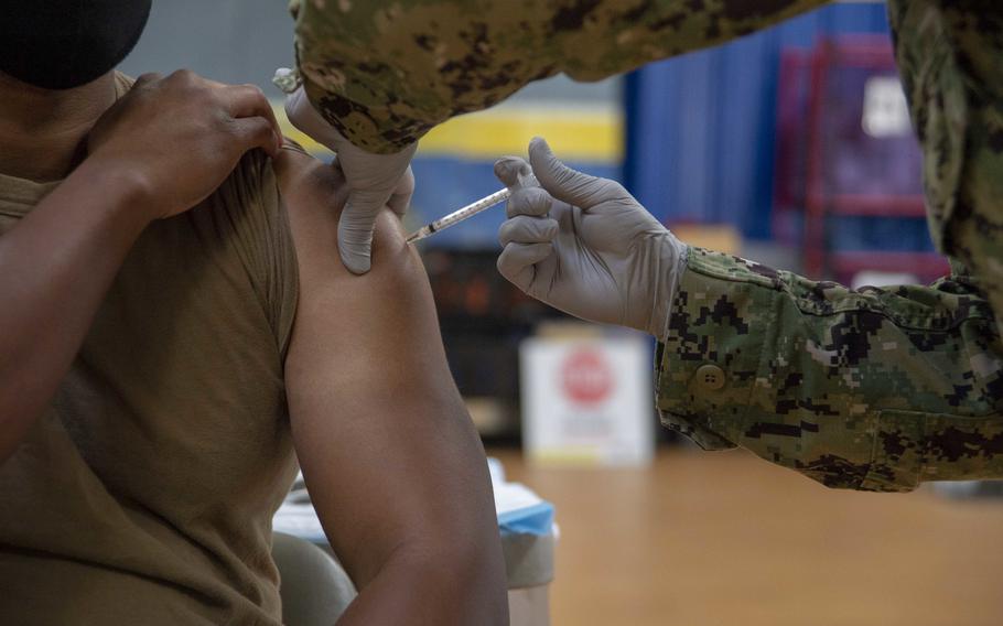 Close-up view of a man’s upper arm as hands with rubber gloves administer a shot.