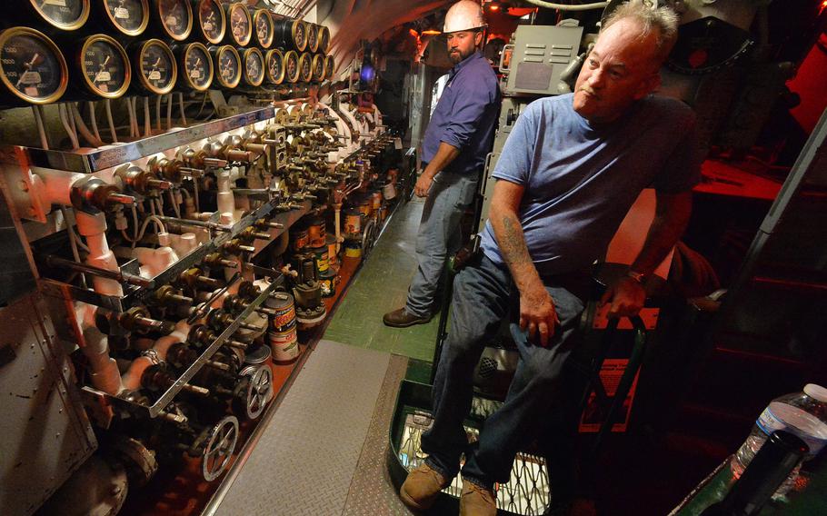 Chief of the boat Darrel Flint, 58, right, pauses while working inside the USS Cod submarine on Aug. 11, 2021, at Donjon Shipbuilding & Repair in Erie. Donjon project manager Matt Ross, 40, is at back. Flint worked on the main air system after a local power outage temporarily stopped repairs.