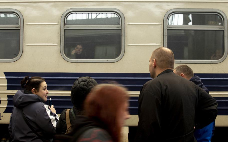 A woman waiting to head home to Kharkiv, Ukraine, sits on a train in Lviv and talks by phone to a friend on the platform, left. 