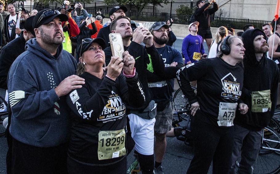 Runners and spectators watch as the Army’s Golden Knights parachute team performs before the Army 10-Miler on Sunday, Oct. 9, 2022, at the Pentagon.