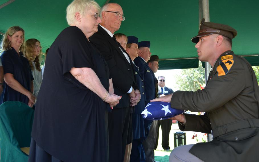 Soldier kneels and gives a folded American flag to a woman who is standing.