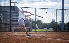 A service member in athletic gear swings a bat.