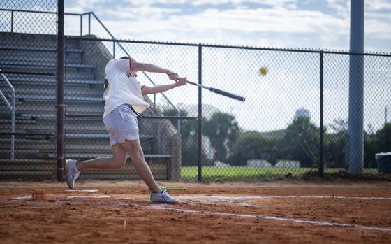 A service member in athletic gear swings a bat.