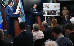 Gen. Dan Caine, on the right at a podium, speaks while Defense Secretary Pete Hegseth looks on from another podium on the left.