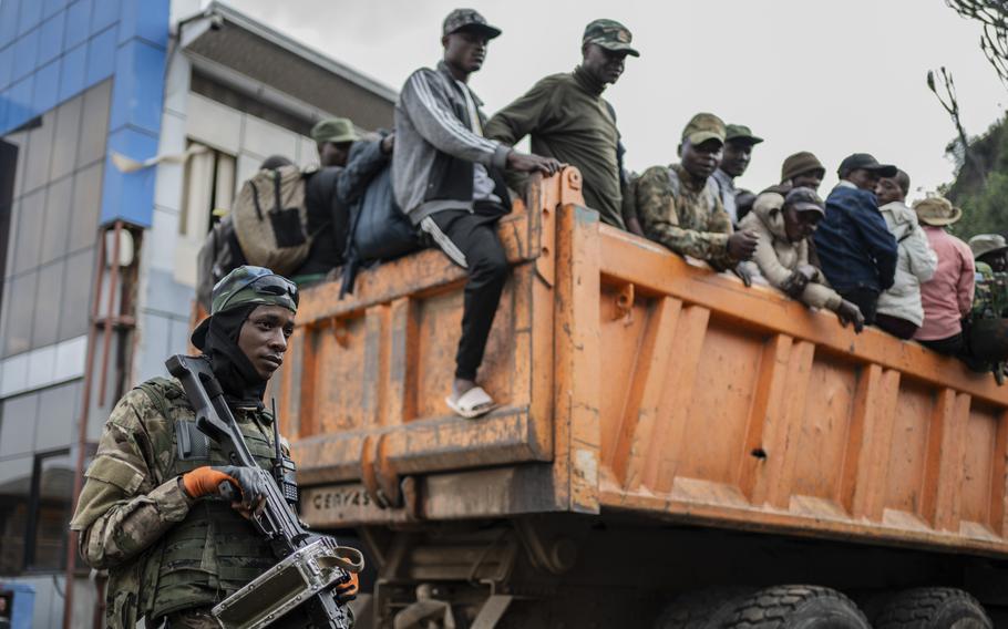 A guard with a gun stands next to a truck filled with men.