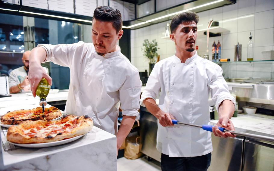 A cook prepares a pizza while another takes on out of the oven.